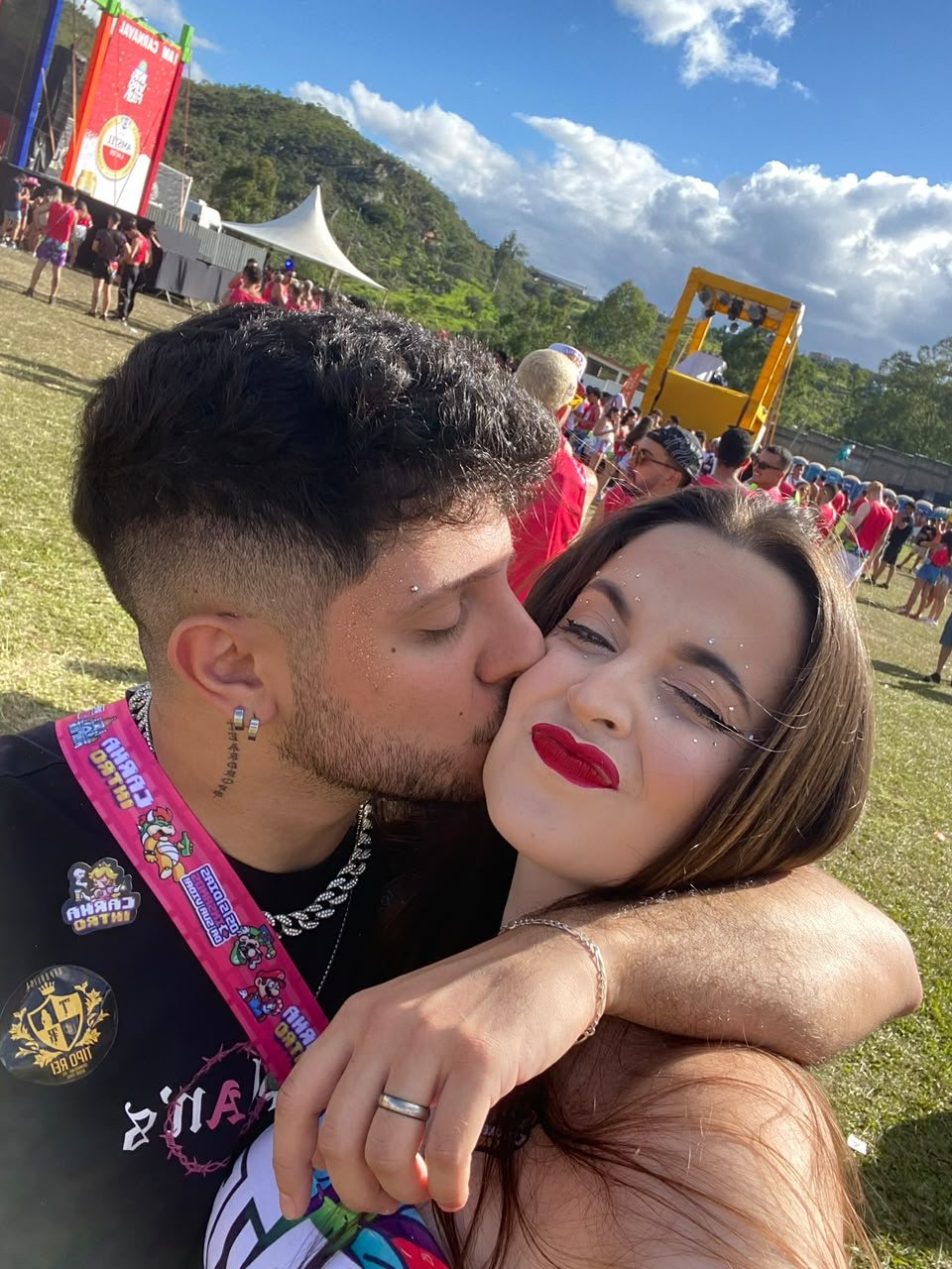 Matheus beijando a bochecha de Marta em bloco de carnaval, ela com glitter no rosto