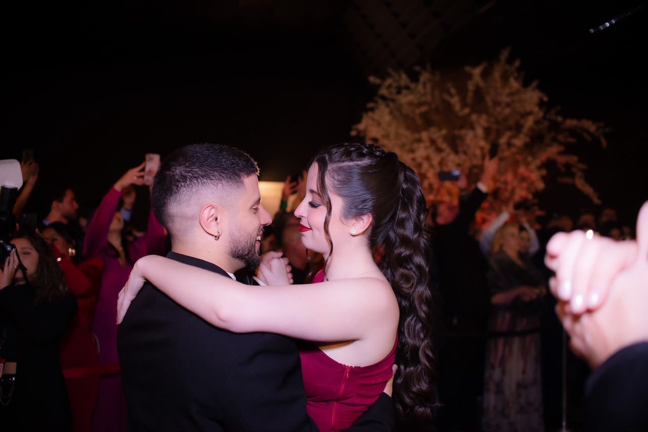 Marta e Matheus dançando abraçados em festa, ela de vestido vinho