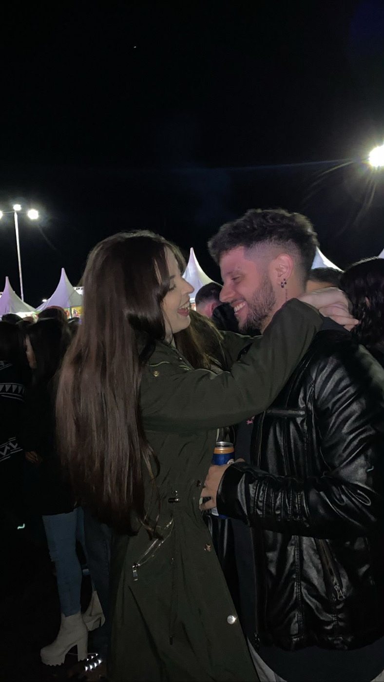 Marta abraçando Matheus, os dois rindo em festival à noite