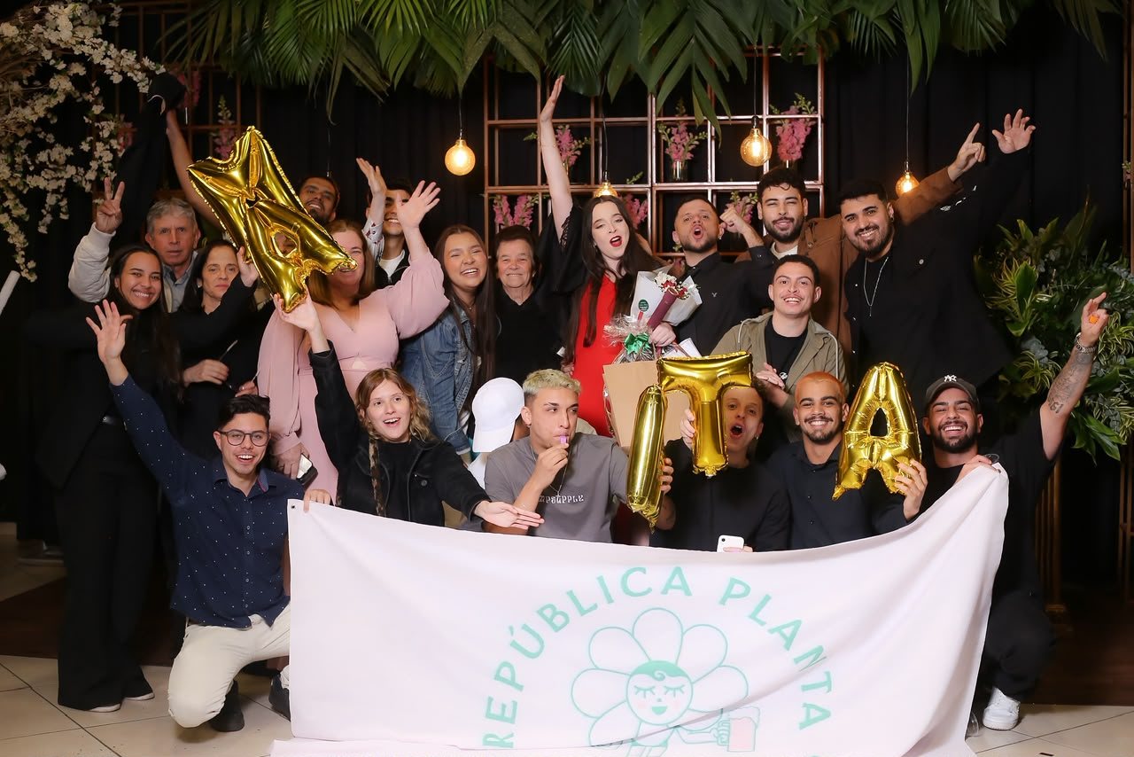 Grupo de família e amigos comemorando a formatura de Marta com balões dourados e faixa