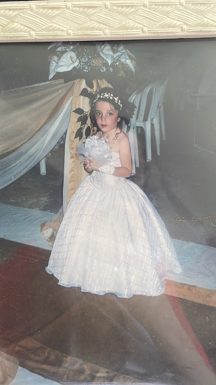 Foto antiga de Marta criança vestida de daminha com vestido branco rodado e buquê
