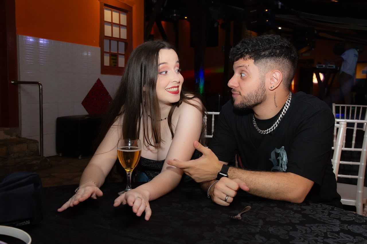 Marta e Matheus fazendo caretas sentados à mesa de uma festa