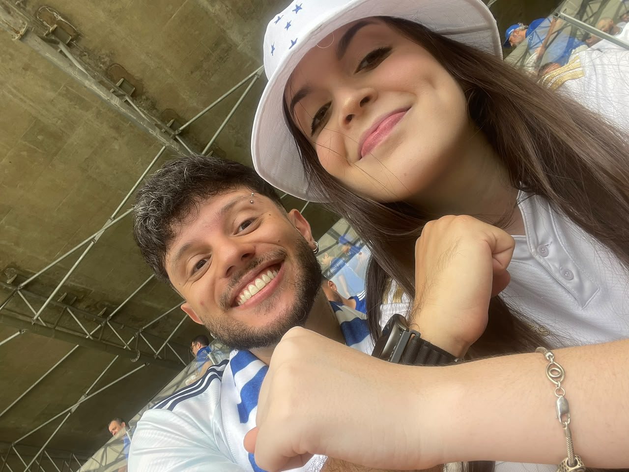 Selfie de Marta e Matheus sorrindo com camisas do Cruzeiro na arquibancada